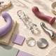 Silicone, glass and stainless steel sex toys displayed on a cream stone surface with lavender accents.