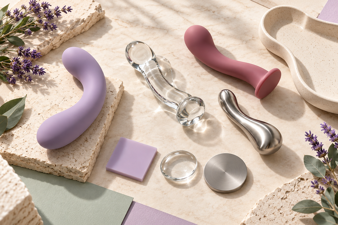 Silicone, glass and stainless steel sex toys displayed on a cream stone surface with lavender accents.
