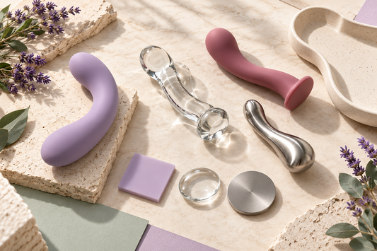 Silicone, glass and stainless steel sex toys displayed on a cream stone surface with lavender accents.