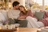 Happy couple cuddling on a cream sofa, holding hands and enjoying a quiet moment together at home.