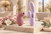 Pink clitoral suction vibrator and lavender rabbit vibrator displayed side by side on a cream stone surface.